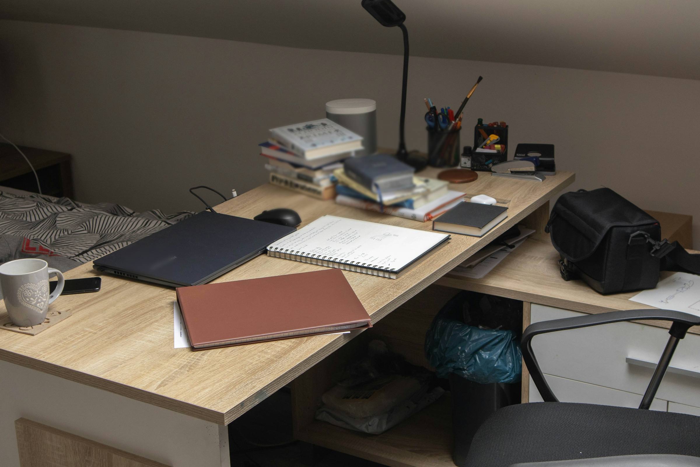 Skrivebord med lukket bærbar, notesbog, kop, bøger og lampe i dæmpet lys